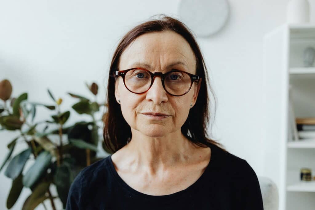 An Elderly Woman Wearing Red Framed Eyeglasses while Seriously Looking at the Camera