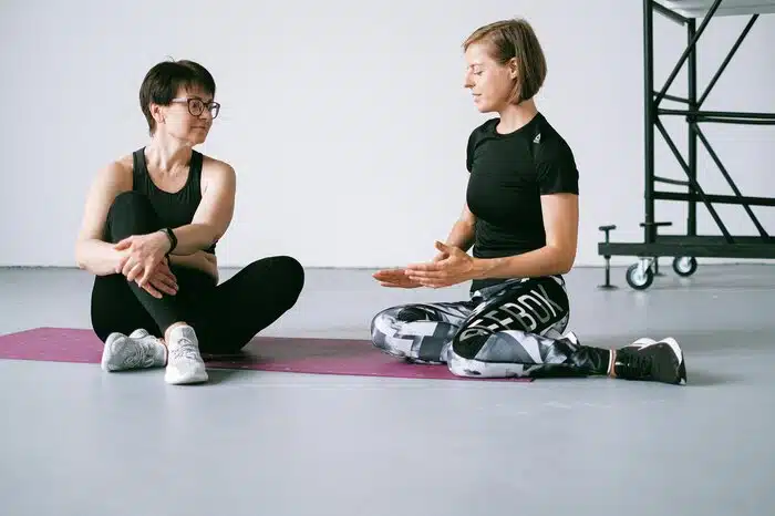 Women in Sportswear Discussing and Sitting on Purple Yoga Mat